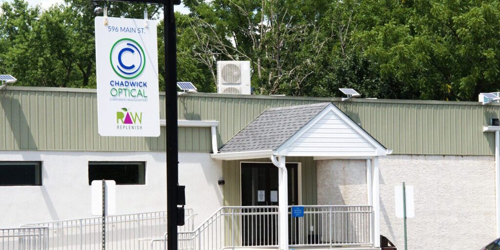 Exterior of Chadwick Optical corporate headquarters, showing a white building with green accents and a hanging sign displaying the company logo.