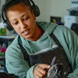lab-staff-2 Li at Chadwick Optical, wearing headphones and a green hoodie, pointing at a lens during the AOL lens casting process.