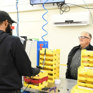 lab-staff-5 Ken and Ralf at Chadwick Optical discuss tasks at a workstation surrounded by yellow trays and tools.