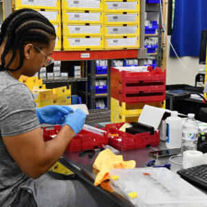 lab-staff-6 Esmerlin at Chadwick Optical organizes parts and prepares lenses at a workstation filled with yellow and red trays.