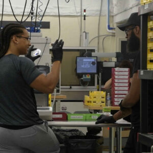 lab-staff-8 Esmerlin (left) and a colleague engage in conversation at Chadwick Optical’s lab, surrounded by equipment and organized trays used for processing lenses.