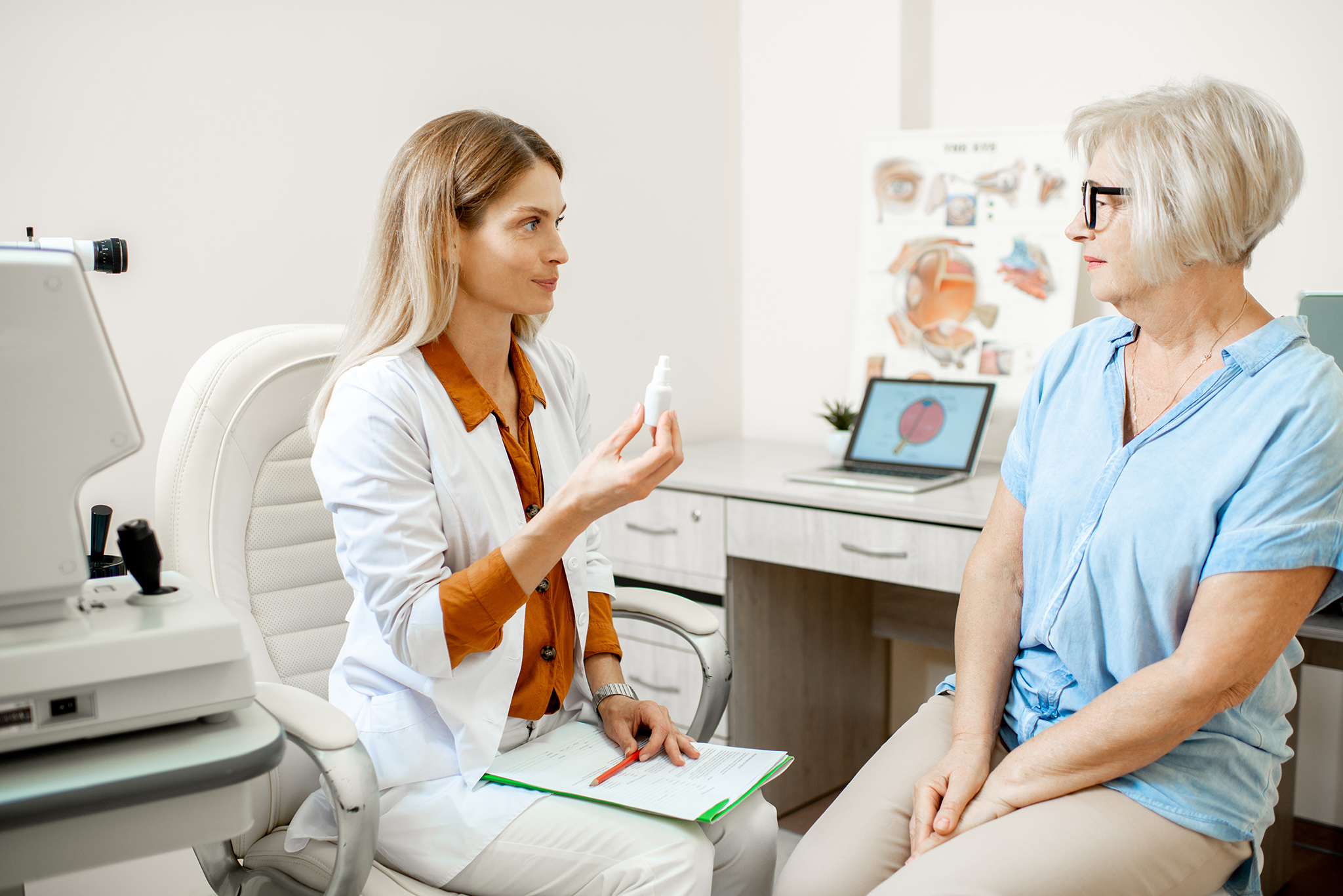 Senior woman patient talking with female ophthalmologist during a medical consultation at the ophthalmologic office. Doctor offering eye medcine for a patient