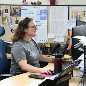 office-staff-7 Michelle at Chadwick Optical, working at her desk and focused on her computer screen, with a background of pinned notes and schedules on the cubicle wall.