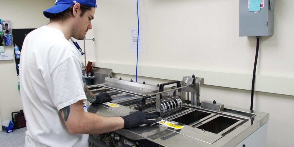 Man in a blue cap and gloves operates an ultrasonic cleaner at Chadwick Optical.